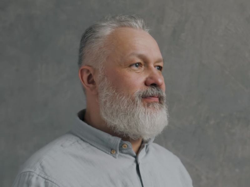 na slici se nalazi čovek sa prosedom dugom bradom u sivoj košulji