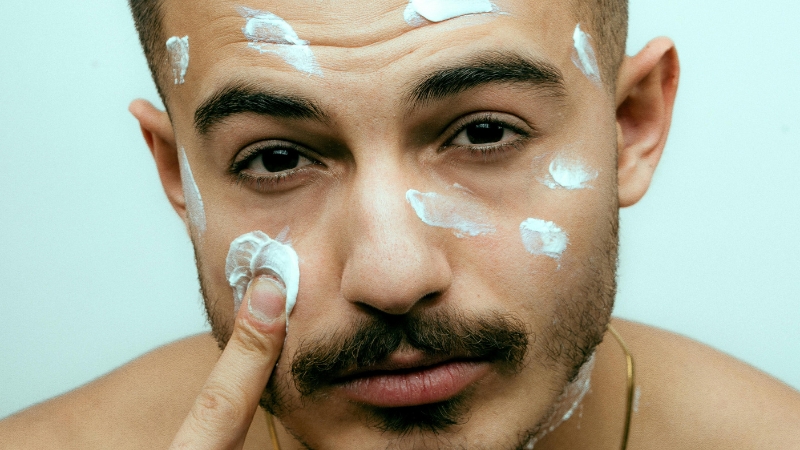 Muškarac nanosi kremu na lice dok su mu na čelu i obrazima vidljivi tragovi preparata za negu kože